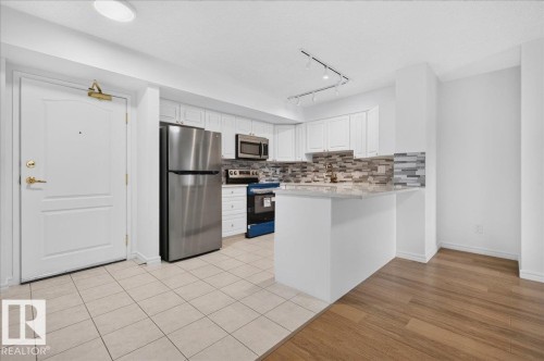 Kitchen featuring white cabinetry, stainless steel appliances, a multi-tone tile backsplash, and a breakfast bar with a light-toned countertop - #1102 10909 103 Av Nw, Edmonton, AB - Indoor Photo Showing Kitchen With Upgraded Kitchen