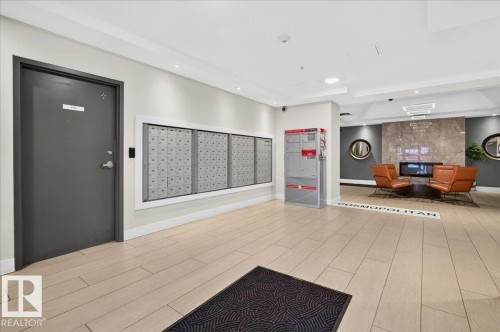 Recessed lighting, wood-finish flooring, built-in mailboxes, and a wall-mounted fireplace with a stone surround - #1102 10909 103 Av Nw, Edmonton, AB - Indoor Photo Showing Other Room