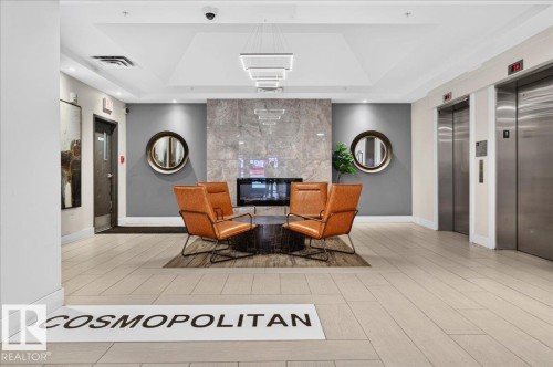 Lobby featuring a stone-clad electric fireplace, modern linear chandeliers, light-toned tile flooring, and two stainless steel elevators - #1102 10909 103 Av Nw, Edmonton, AB - Indoor Photo Showing Other Room