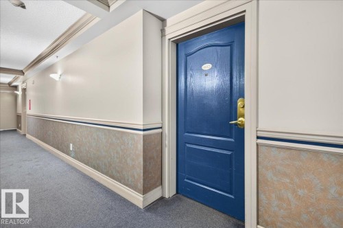 Corridor with carpet flooring, wall sconces, textured wainscoting, crown molding, and a paneled entry door - #1102 10909 103 Av Nw, Edmonton, AB - Indoor Photo Showing Other Room