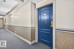 Corridor with carpet flooring, wall sconces, textured wainscoting, crown molding, and a paneled entry door - 