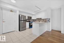 Kitchen featuring white cabinetry, stainless steel appliances, a multi-tone tile backsplash, and a breakfast bar with a light-toned countertop - 