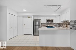 White cabinetry with gold-tone hardware, stainless steel appliances, a tiled backsplash, and a breakfast bar with a solid surface countertop - 