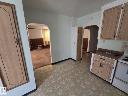 Cabinetry with decorative paneling and white trim, patterned floor tiles, arched doorways, a built-in pantry cabinet, and light-colored walls - 9839 81 Avenue Nw, Edmonton, AB - Indoor Photo Showing Kitchen
