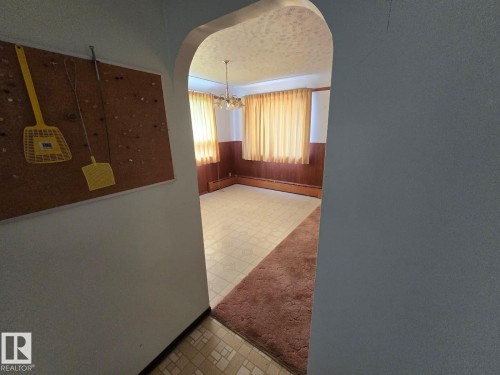 Arched doorway opening to a room featuring wood paneling, multiple windows, a ceiling-mounted light fixture, and tile flooring - 9839 81 Avenue Nw, Edmonton, AB - Indoor Photo Showing Other Room
