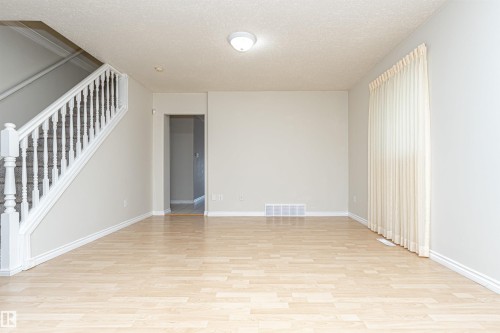 Light wood-finish flooring, staircase with white spindles, neutral wall color, and window with vertical blinds - 12241 93 Street Nw, Edmonton, AB - Indoor Photo Showing Other Room