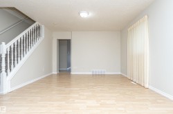 Light wood-finish flooring, staircase with white spindles, neutral wall color, and window with vertical blinds - 