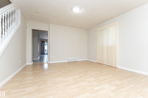 Hardwood-style flooring throughout, staircase with white balusters, light neutral wall colors, and a window with vertical blinds - 12241 93 Street Nw, Edmonton, AB - Indoor Photo Showing Other Room