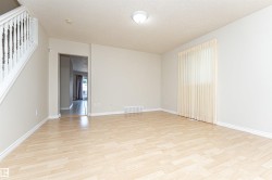 Hardwood-style flooring throughout, staircase with white balusters, light neutral wall colors, and a window with vertical blinds - 