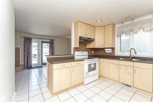 Kitchen featuring light wood-finish cabinetry, solid surface countertops, a tile backsplash, and stainless steel sink - 12241 93 Street Nw, Edmonton, AB - Indoor Photo Showing Kitchen With Double Sink