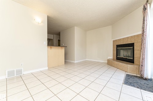 Tile flooring, corner fireplace with tile surround, built-in breakfast bar, wall sconce lighting - 12241 93 Street Nw, Edmonton, AB - Indoor With Fireplace