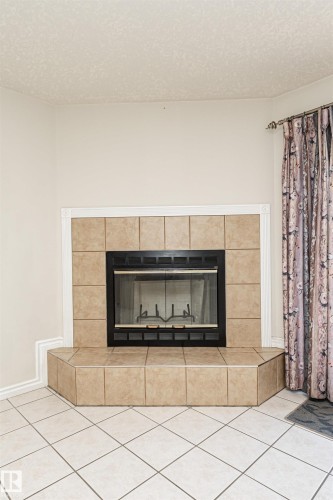 Corner fireplace with a tiled surround and hearth, featuring a black firebox and glass doors - 12241 93 Street Nw, Edmonton, AB - Indoor Photo Showing Other Room With Fireplace