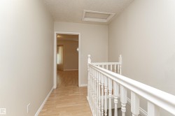 Neutral wall finishes, wood-finish flooring, white painted railing, and an attic access panel - 