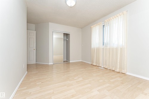 Light wood-finish flooring, a window with sheer curtains, a mirrored closet, and a white ceiling light fixture - 12241 93 Street Nw, Edmonton, AB - Indoor Photo Showing Other Room
