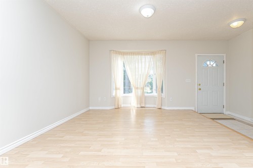 Light wood-finish flooring with a tile entry, a white front door featuring a decorative window, and a bay window - 12241 93 Street Nw, Edmonton, AB - Indoor Photo Showing Other Room