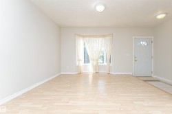 Light wood-finish flooring with a tile entry, a white front door featuring a decorative window, and a bay window - 