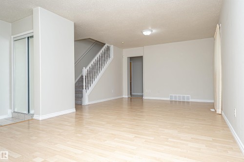 Light wood-finish flooring, staircase with carpeted treads and white banister, overhead flush mount lighting, sliding closet doors with frosted panels, and neutral wall tones - 12241 93 Street Nw, Edmonton, AB - Indoor Photo Showing Other Room