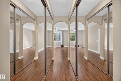 Mirrored sliding closet doors reflecting a spacious room with wood-finish flooring, light-toned walls, and arched doorways - #401 10178 117 St Nw, Edmonton, AB - Indoor Photo Showing Other Room