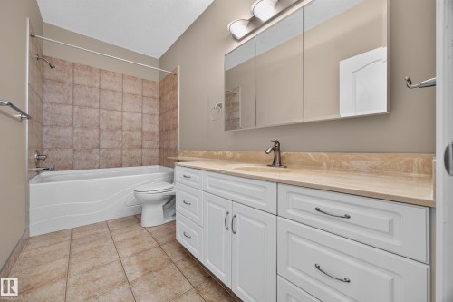 Bathroom featuring a white vanity with paneling and dark hardware, a beige countertop with an integrated sink, and an overhead mirrored medicine cabinet - #401 10178 117 St Nw, Edmonton, AB - Indoor Photo Showing Bathroom