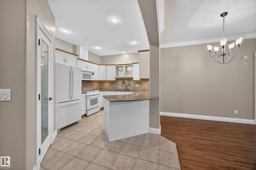 Spacious kitchen featuring white cabinetry, a peninsula with a countertop, integrated white appliances, and tiled flooring - #401 10178 117 St Nw, Edmonton, AB - Indoor Photo Showing Kitchen