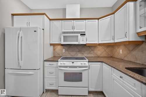 Kitchen featuring white cabinetry with wood-finish trim, a tiled backsplash, and stone-finish countertops - #401 10178 117 St Nw, Edmonton, AB - Indoor Photo Showing Kitchen