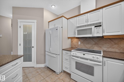 Kitchen featuring white cabinetry, brown granite-finish countertops, and a tiled backsplash - #401 10178 117 St Nw, Edmonton, AB - Indoor Photo Showing Kitchen