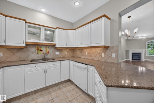 Kitchen featuring white cabinetry with wood-finish trim, speckled countertops, tile flooring, and a tile backsplash - #401 10178 117 St Nw, Edmonton, AB - Indoor Photo Showing Kitchen With Double Sink