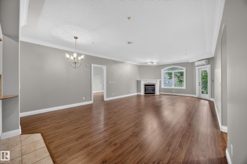 Spacious living area featuring wood-finish flooring, a decorative fireplace with a white mantel, and an arched window - #401 10178 117 St Nw, Edmonton, AB - Indoor With Fireplace