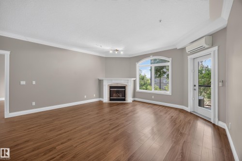Spacious interior featuring wood-finish flooring, a white mantel fireplace, and an arched window - #401 10178 117 St Nw, Edmonton, AB - Indoor Photo Showing Living Room With Fireplace
