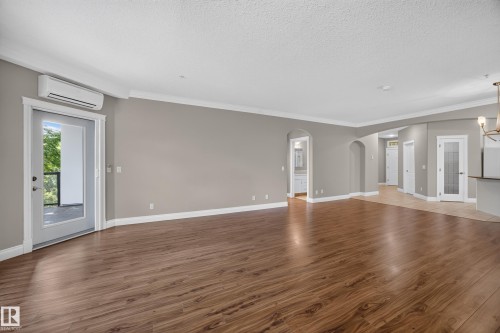 Spacious living area featuring wood-finish flooring, neutral wall tones, crown molding, and a split-system air conditioning unit - #401 10178 117 St Nw, Edmonton, AB - Indoor