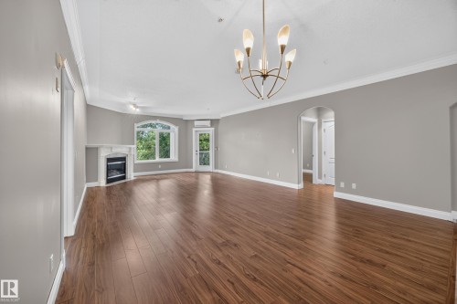 Spacious living area featuring wood-finish flooring, a corner fireplace with a white mantel, an arched window, and a glass-paneled door - #401 10178 117 St Nw, Edmonton, AB - Indoor With Fireplace