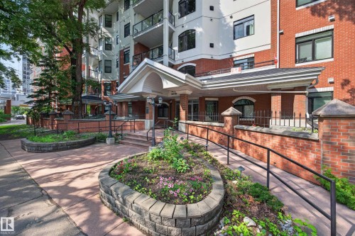Brick facade building featuring a covered entryway, decorative iron fencing, a sloped access ramp, and planted garden beds - #401 10178 117 St Nw, Edmonton, AB - Outdoor With Deck Patio Veranda
