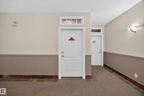 Hallway featuring two-tone walls with a chair rail, white paneled doors with transom windows, and a combination of carpet and natural stone tile flooring - #401 10178 117 St Nw, Edmonton, AB - Indoor Photo Showing Other Room