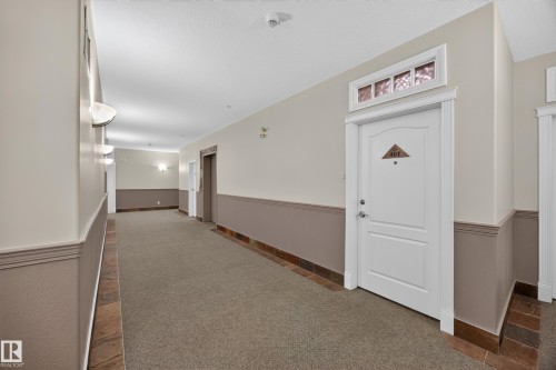 Building corridor with carpet flooring, stone tile borders, and neutral wall tones with chair rail molding - #401 10178 117 St Nw, Edmonton, AB - Indoor Photo Showing Other Room