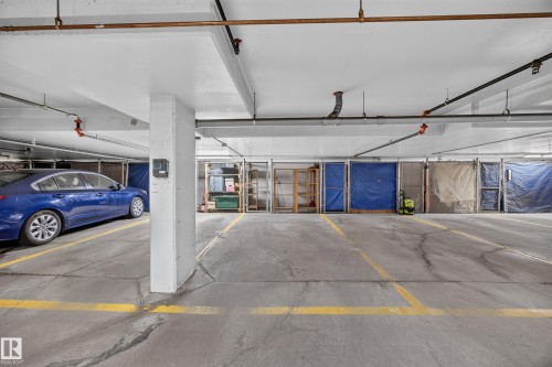 Dedicated parking space within a concrete garage featuring exposed piping and overhead lighting - #401 10178 117 St Nw, Edmonton, AB - Indoor Photo Showing Garage