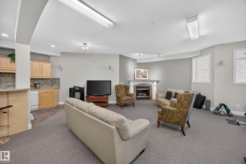 Spacious carpeted room featuring a built-in wet bar with wood cabinetry and a tile backsplash - #401 10178 117 St Nw, Edmonton, AB - Indoor With Fireplace
