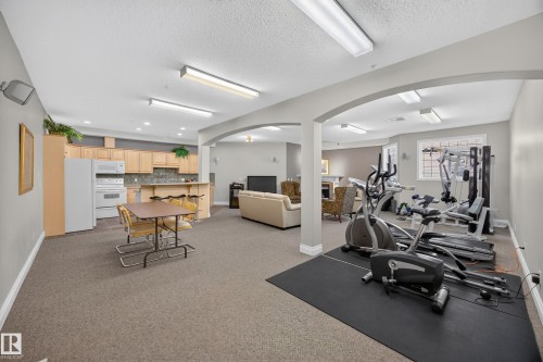 Spacious lower level featuring a full kitchen with light wood cabinetry, stone-finish backsplash, and white appliances - #401 10178 117 St Nw, Edmonton, AB - Indoor Photo Showing Gym Room