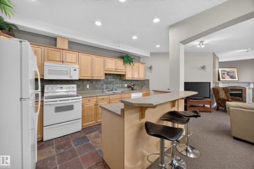 Open-concept kitchen featuring light wood cabinetry, stone-look tile backsplash, and a breakfast bar - #401 10178 117 St Nw, Edmonton, AB - Indoor Photo Showing Kitchen With Fireplace