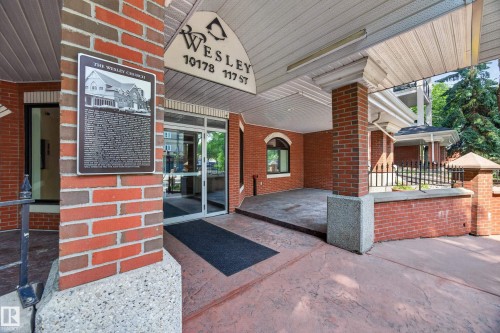 Building entrance featuring a brick facade, glass double doors, a prominent overhead awning, and a black wrought iron fence - #401 10178 117 St Nw, Edmonton, AB - Outdoor With Exterior