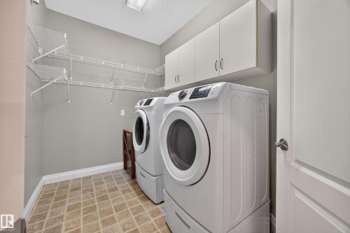 Dedicated laundry area featuring a front-load washer and dryer, upper cabinetry, extensive wire shelving, and tiled flooring - #401 10178 117 St Nw, Edmonton, AB - Indoor Photo Showing Laundry Room