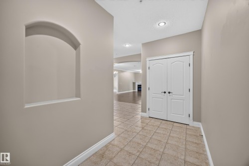 Entrance hallway featuring tile flooring, a built-in arched wall niche, recessed lighting, and double bi-fold doors - #401 10178 117 St Nw, Edmonton, AB - Indoor Photo Showing Other Room