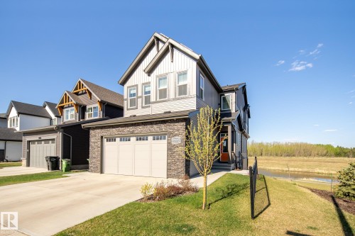 Two-story property with a two-car garage, stone and siding exterior, an orange entry door, and a concrete driveway - 7135 Edgemont Way Nw, Edmonton, AB 
