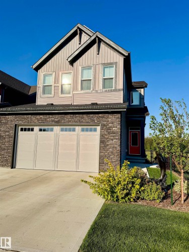 Multi-level facade with a red entry door, an integrated two-car garage, and stone-finish siding - 7135 Edgemont Way Nw, Edmonton, AB 