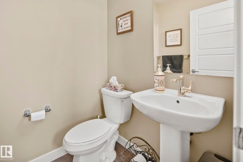 Pedestal sink with polished chrome faucet, white toilet, and wood-finish flooring - 7135 Edgemont Way Nw, Edmonton, AB 