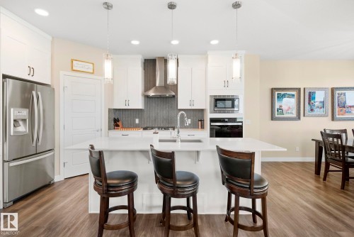 Well-appointed kitchen featuring stainless steel appliances, white cabinetry, a large center island, pendant lighting, and wood-finish flooring - 7135 Edgemont Way Nw, Edmonton, AB 