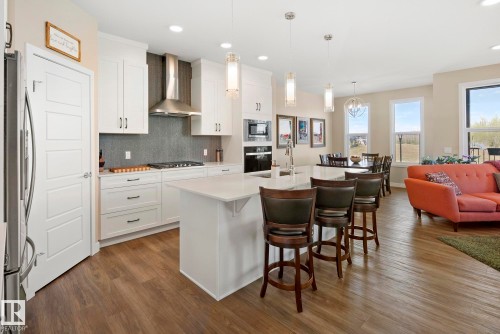 Open-concept kitchen featuring white cabinetry, stainless steel appliances, a center island with countertop seating, and wood-finish flooring - 7135 Edgemont Way Nw, Edmonton, AB 