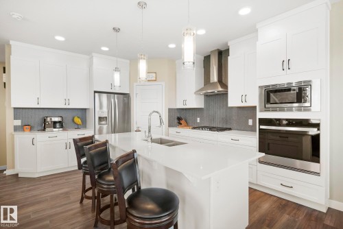 Kitchen featuring white cabinetry, a large center island, stainless steel appliances, and wood-finish flooring - 7135 Edgemont Way Nw, Edmonton, AB 
