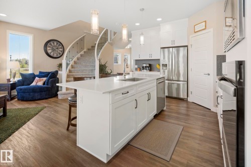Open-concept living space with wood-finish flooring, a spiral staircase, white kitchen cabinetry, stainless steel appliances, and a kitchen island with seating - 7135 Edgemont Way Nw, Edmonton, AB 