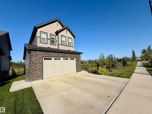 Two-story residence featuring a stone-clad garage with a paneled door, horizontal siding, and multiple windows - 7135 Edgemont Way Nw, Edmonton, AB 