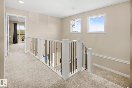 Spacious landing with neutral carpeting, white baluster railing with black metal spindles, and a contemporary ceiling light fixture - 7135 Edgemont Way Nw, Edmonton, AB 